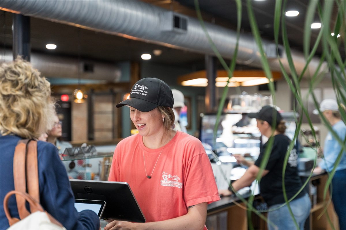 Taylor laughing with a guest at the register in a DT's cap and shirt